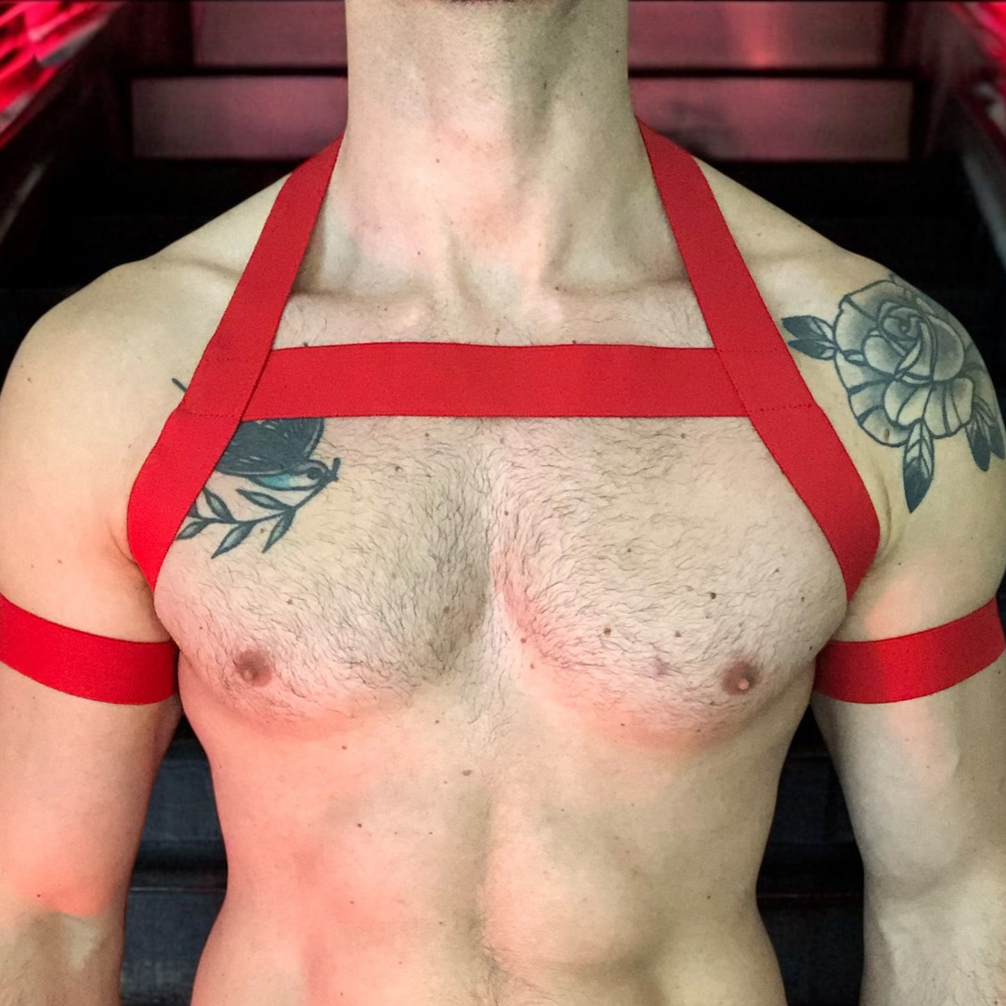 Model wearing a custom-made red elastic chest harness and black mesh jockstrap by Cheeky Boy Harness. Made-to-measure men's festival and clubwear set designed for pride, circuit parties, and dance events